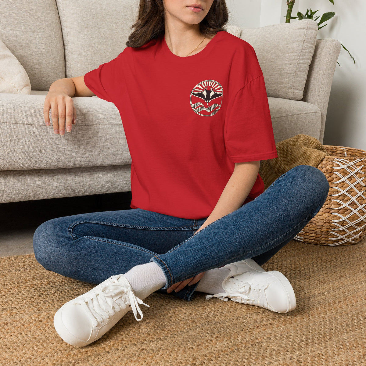 Woman sitting on the floor in a red t-shirt with a small manta ray sunrise badge on the chest, digital mockup
