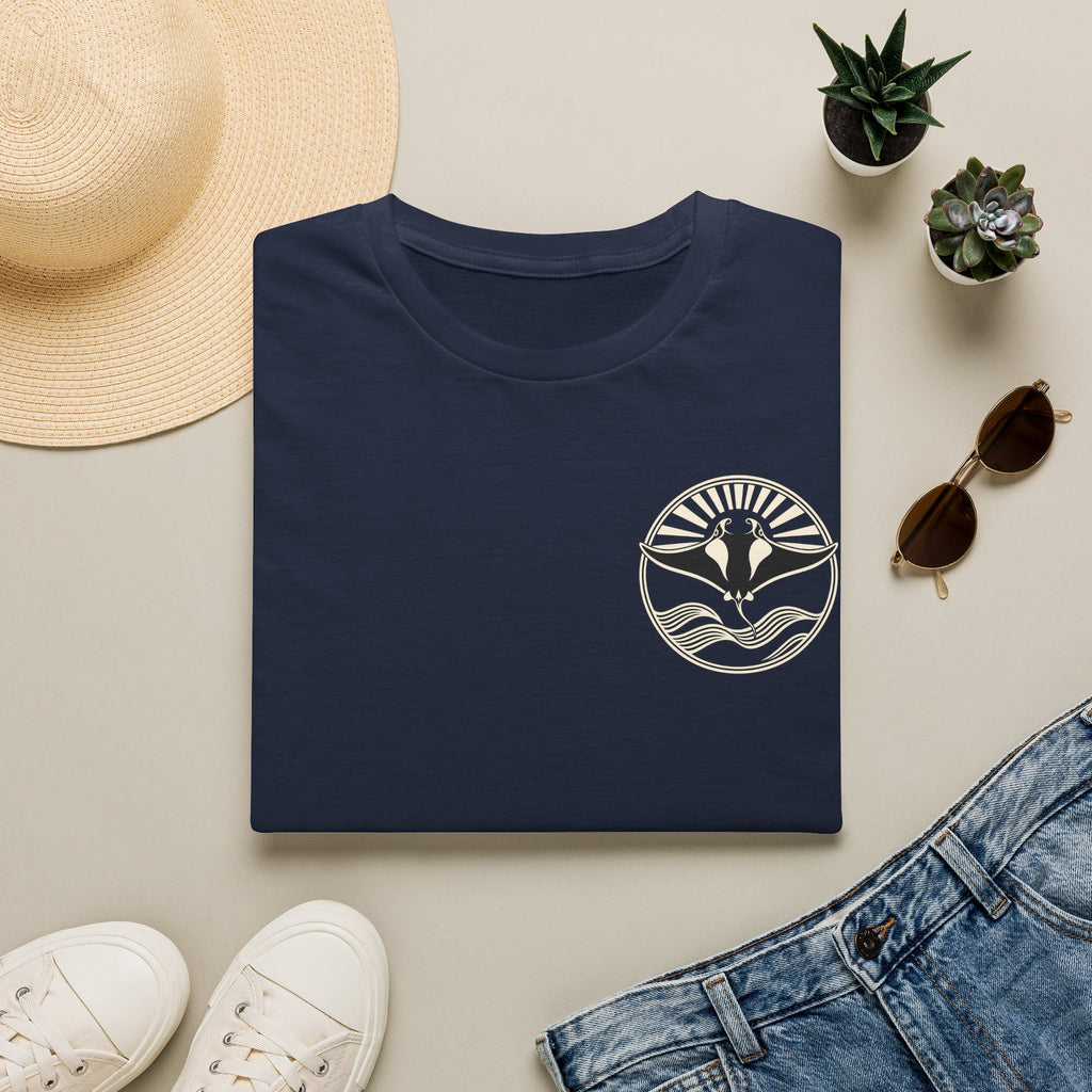 Folded navy t-shirt showing the small manta ray sunrise badge on the chest, flat lay with sunglasses and jeans