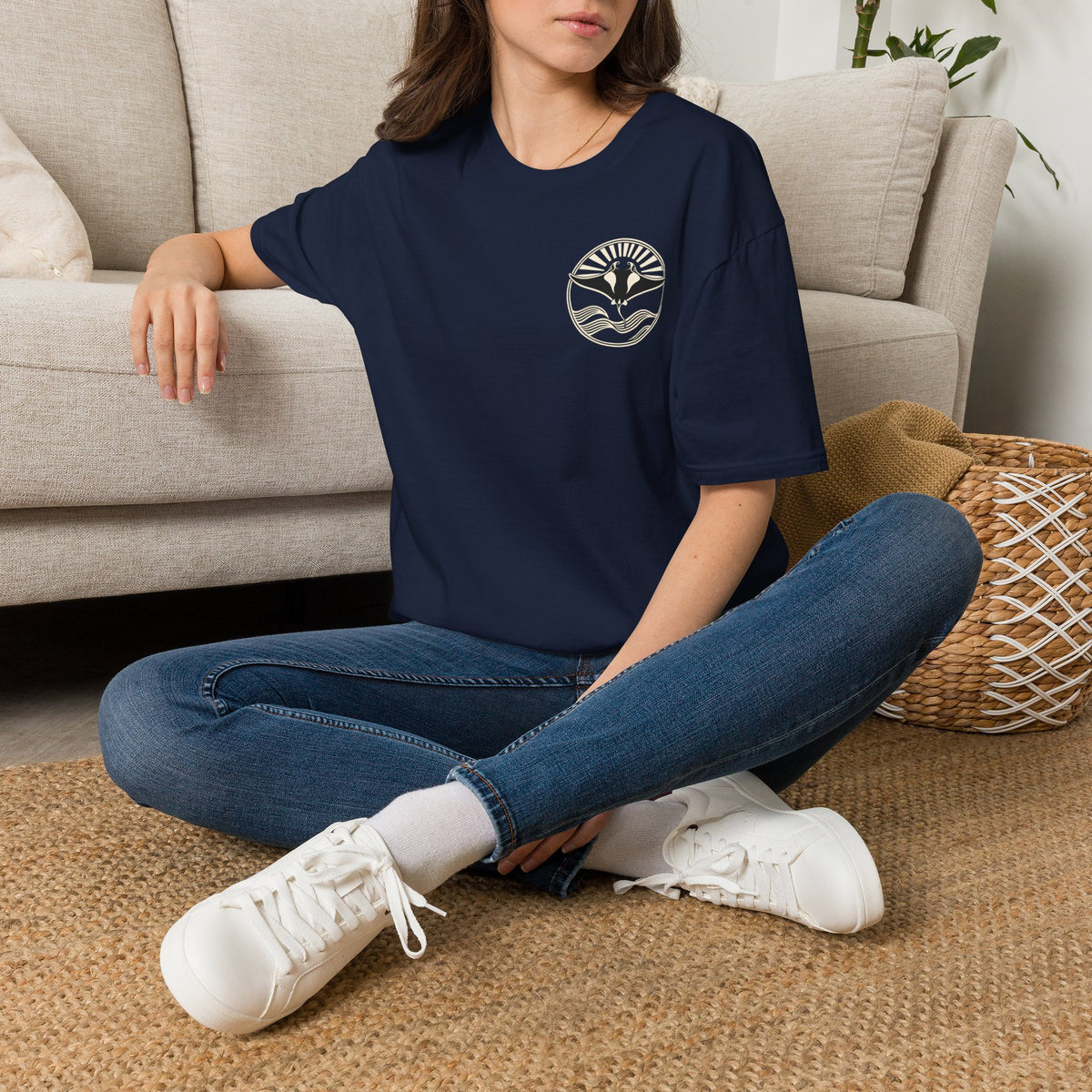 Woman sitting on the floor in a navy t-shirt with a small manta ray sunrise badge on the chest, digital mockup