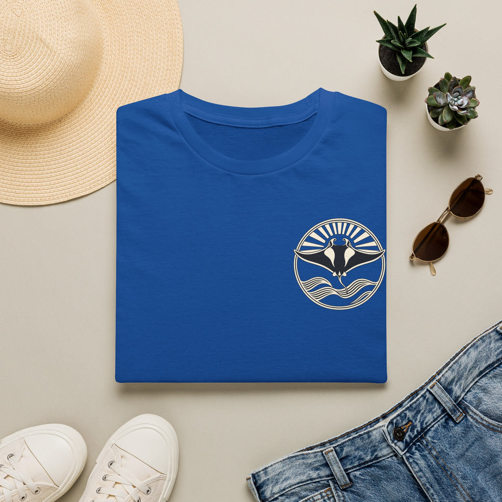 Folded royal blue t-shirt showing the small manta ray sunrise badge on the chest, flat lay with sunglasses and jeans