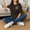 Woman sitting on the floor in a dark chocolate t-shirt with a small manta ray sunrise badge on the chest, digital mockup