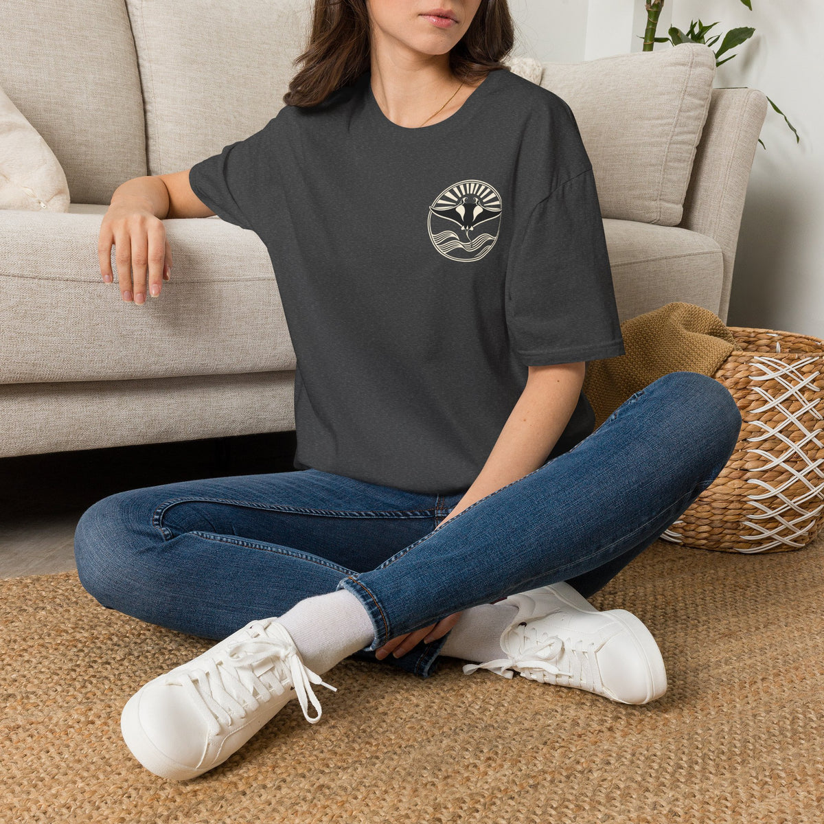Woman sitting on the floor in a dark heather grey t-shirt with a small manta ray sunrise badge on the chest, digital mockup