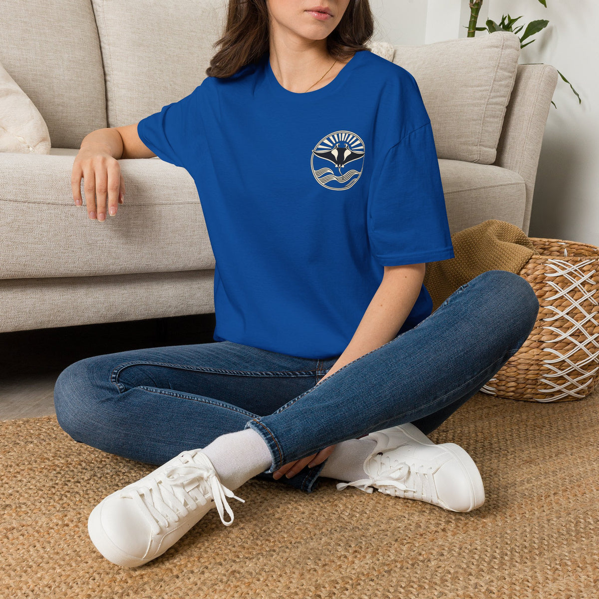 Woman sitting on the floor in a royal blue t-shirt with a small manta ray sunrise badge on the chest, digital mockup