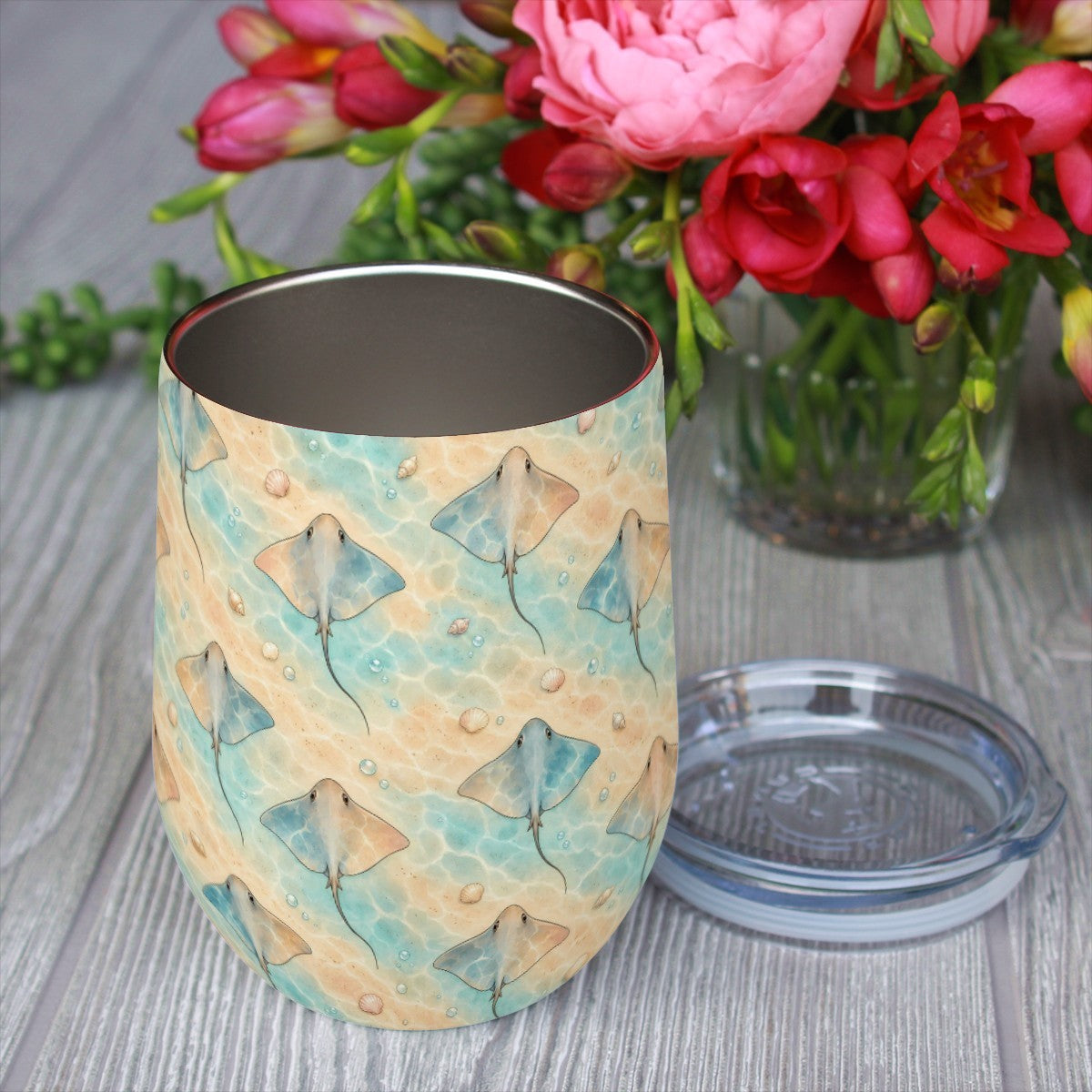 Stingray pattern tumbler with its clear lid beside it on a wooden table, red flowers in the background