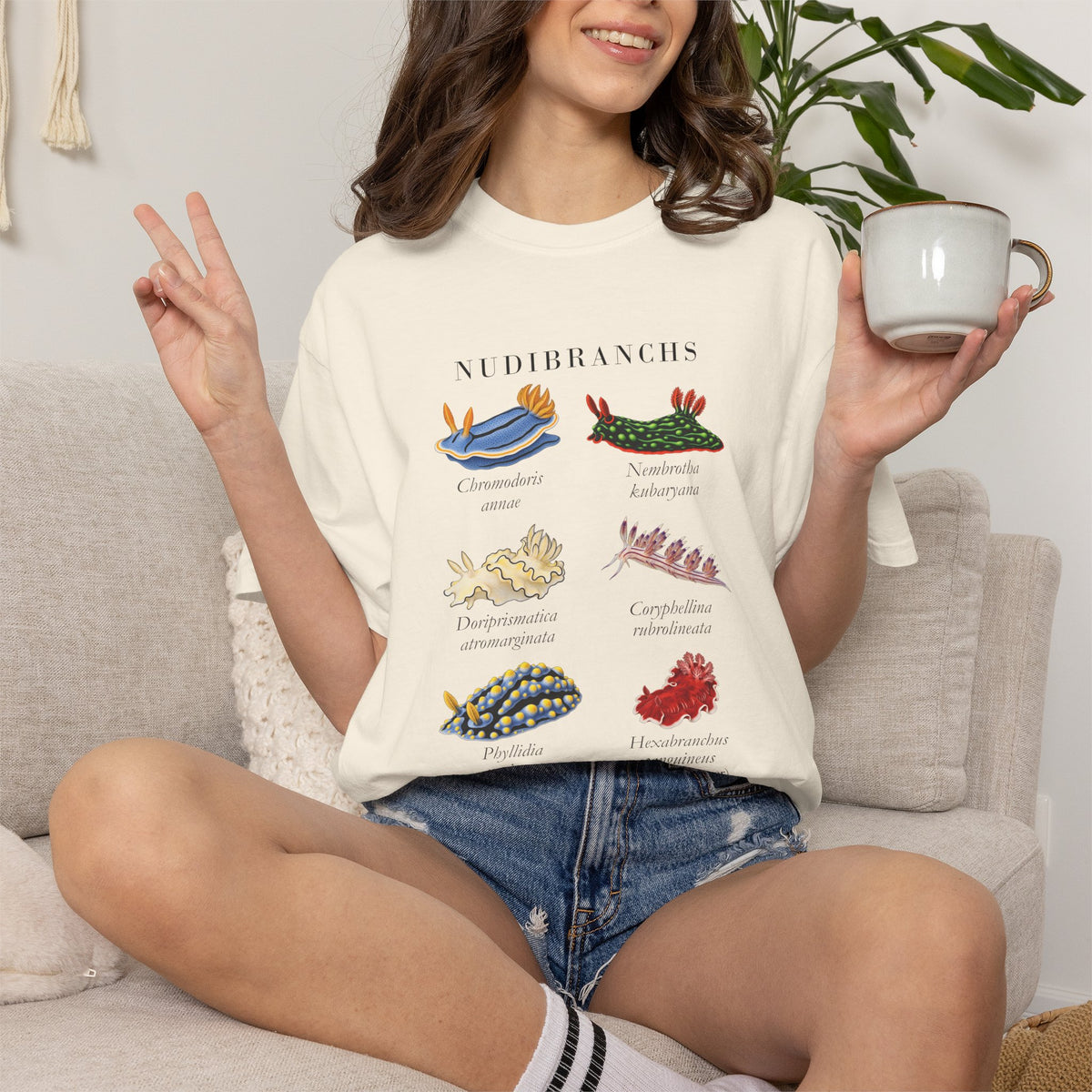 Ivory nudibranch plate tee on a seated model making a peace sign and holding a mug