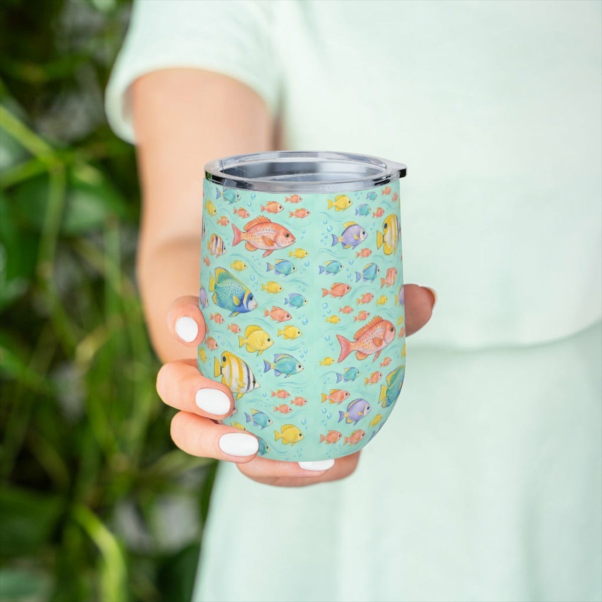 Hand holding the reef fish pattern tumbler in front of green leaves, with a pale green top behind