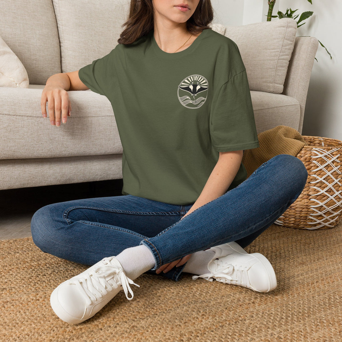 Woman sitting on the floor in a military green t-shirt with a small manta ray sunrise badge on the chest, digital mockup