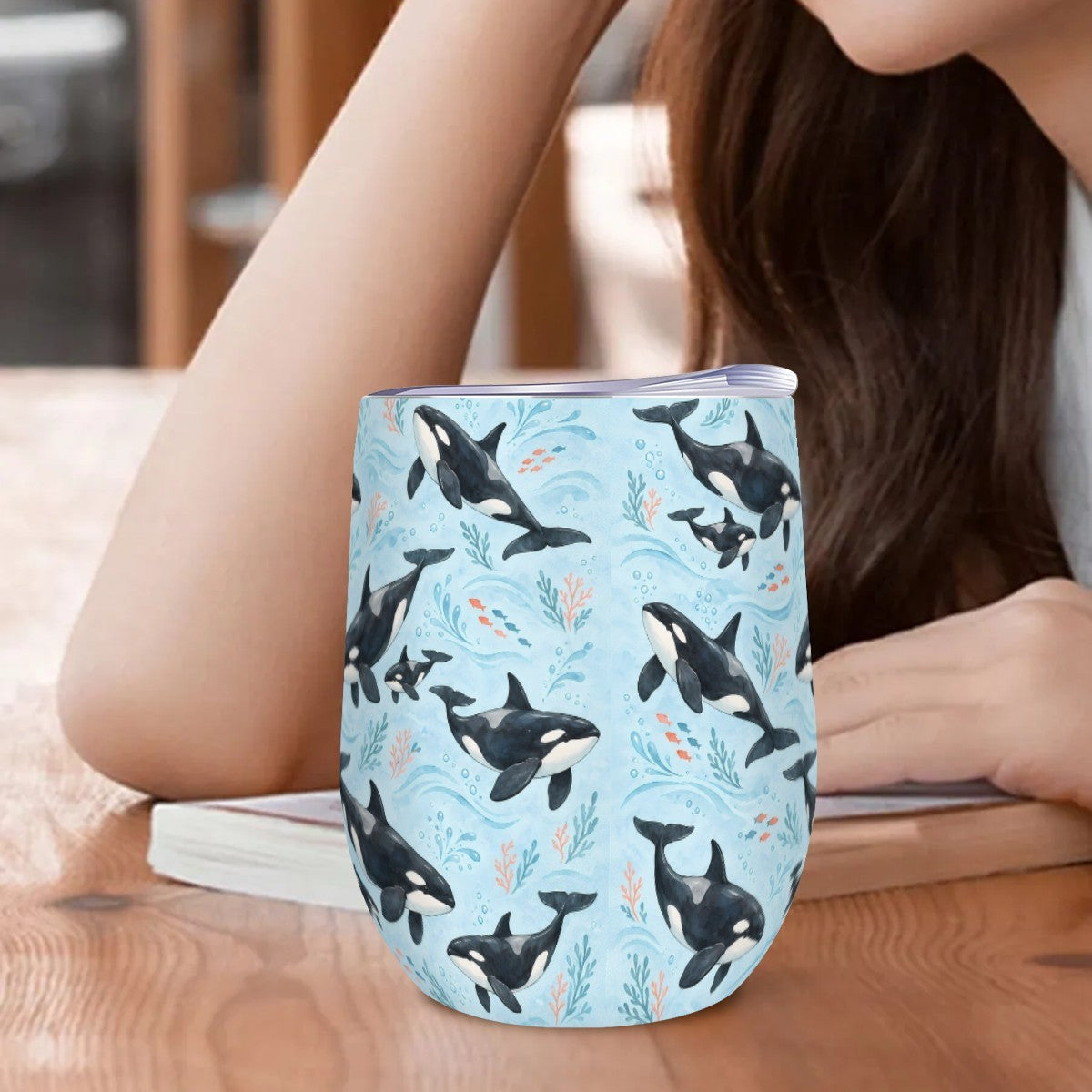 Orca tumbler standing on a wooden table beside a woman resting her arm