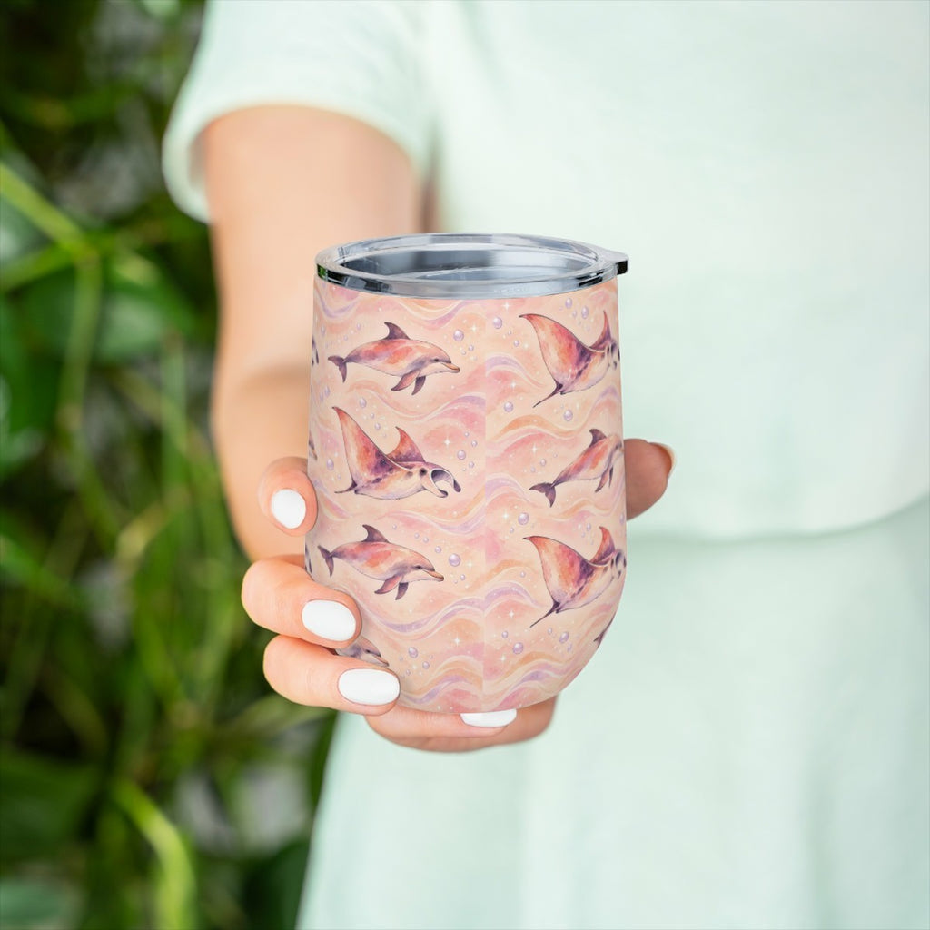 Hand holding the dolphin and ray pattern tumbler in front of green leaves, with a pale green top behind