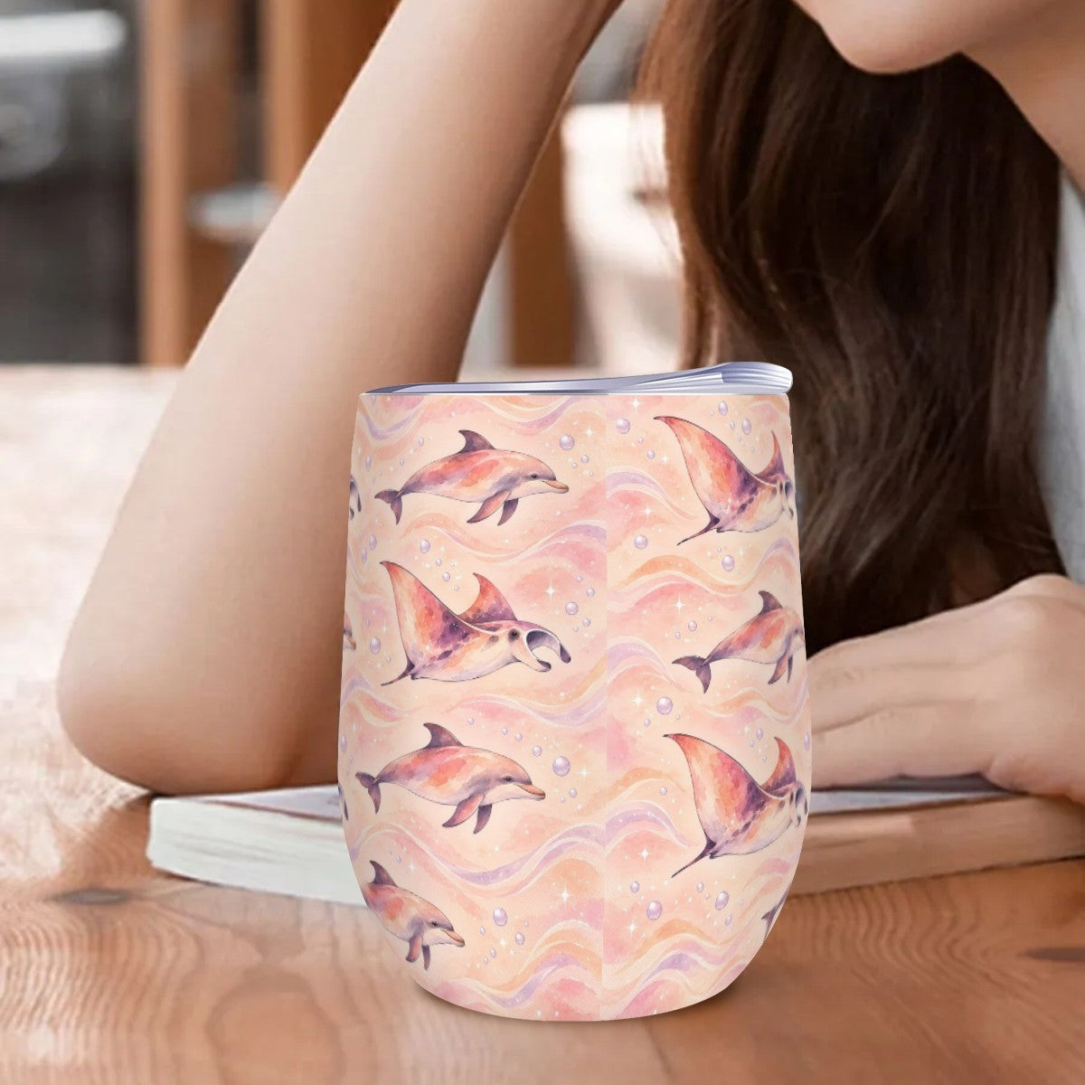 Dolphin and ray tumbler standing on a wooden table beside a woman resting her arm