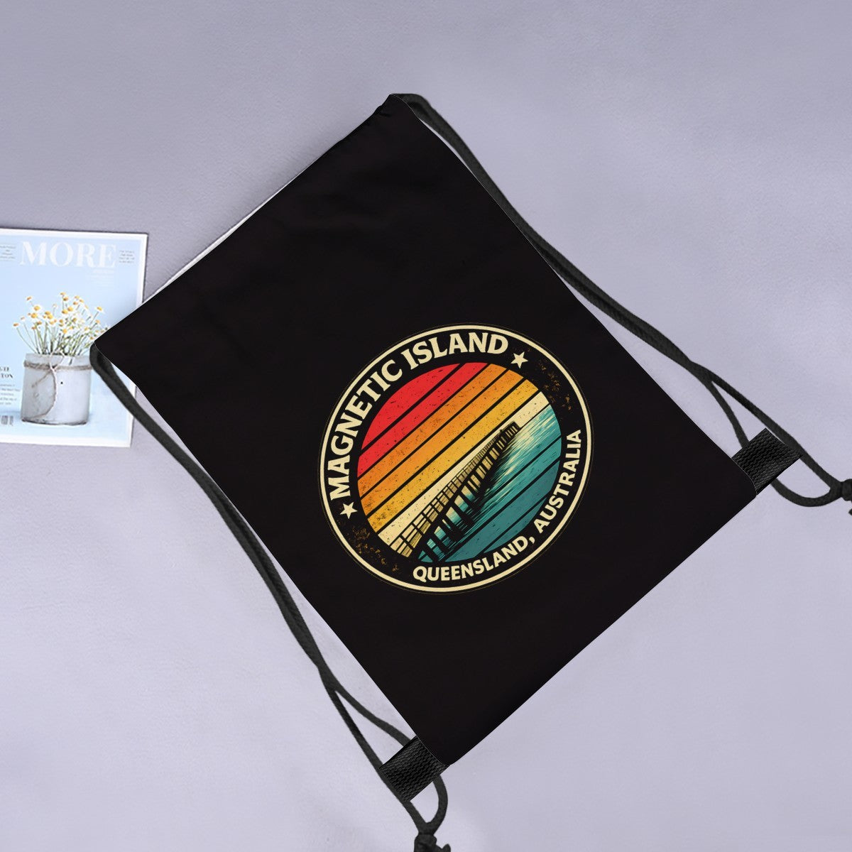 Retro Magnetic Island Pier drawstring bag laid flat next to a magazine and flowers.