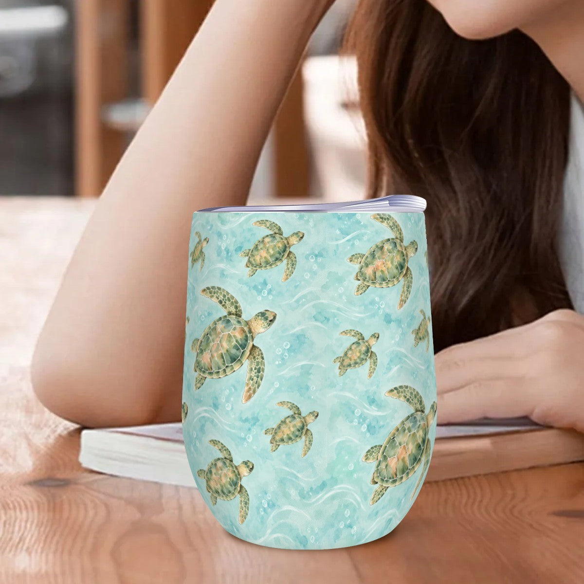 Sea turtle tumbler standing on a wooden table beside a woman resting her arm