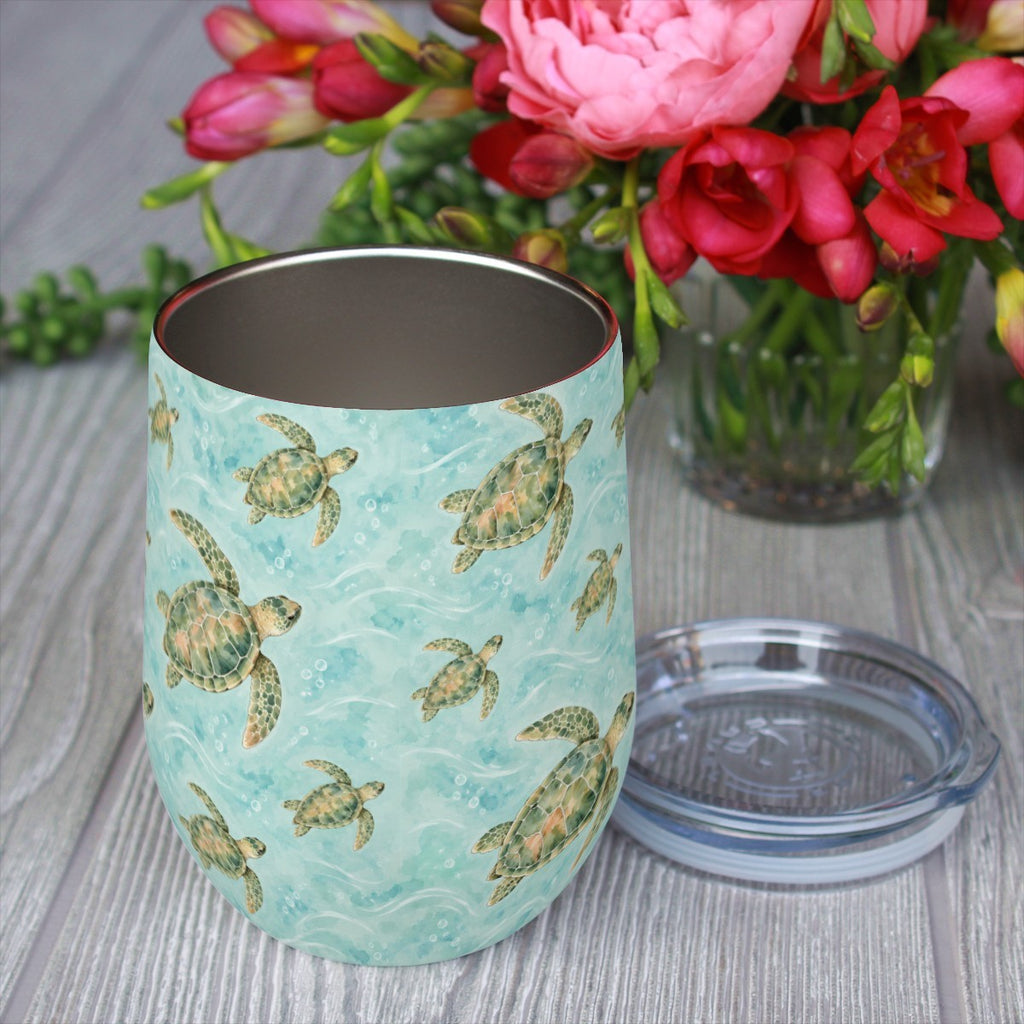 Sea turtle pattern tumbler with its clear lid beside it on a wooden table, red flowers in the background