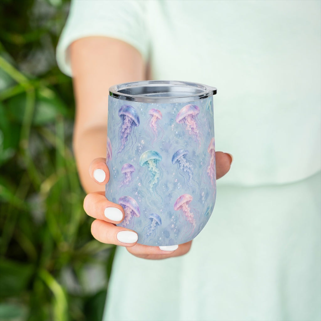 Hand holding the jellyfish pattern tumbler in front of green leaves, with a pale green top behind