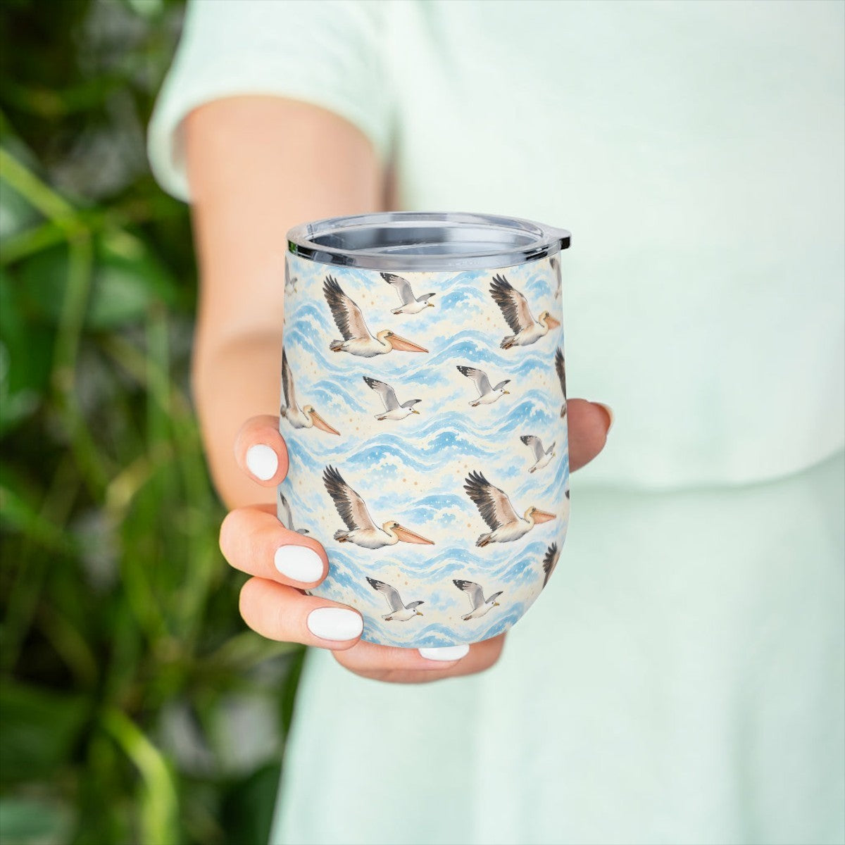 Hand holding the pelican pattern tumbler in front of green leaves, with a pale green top behind