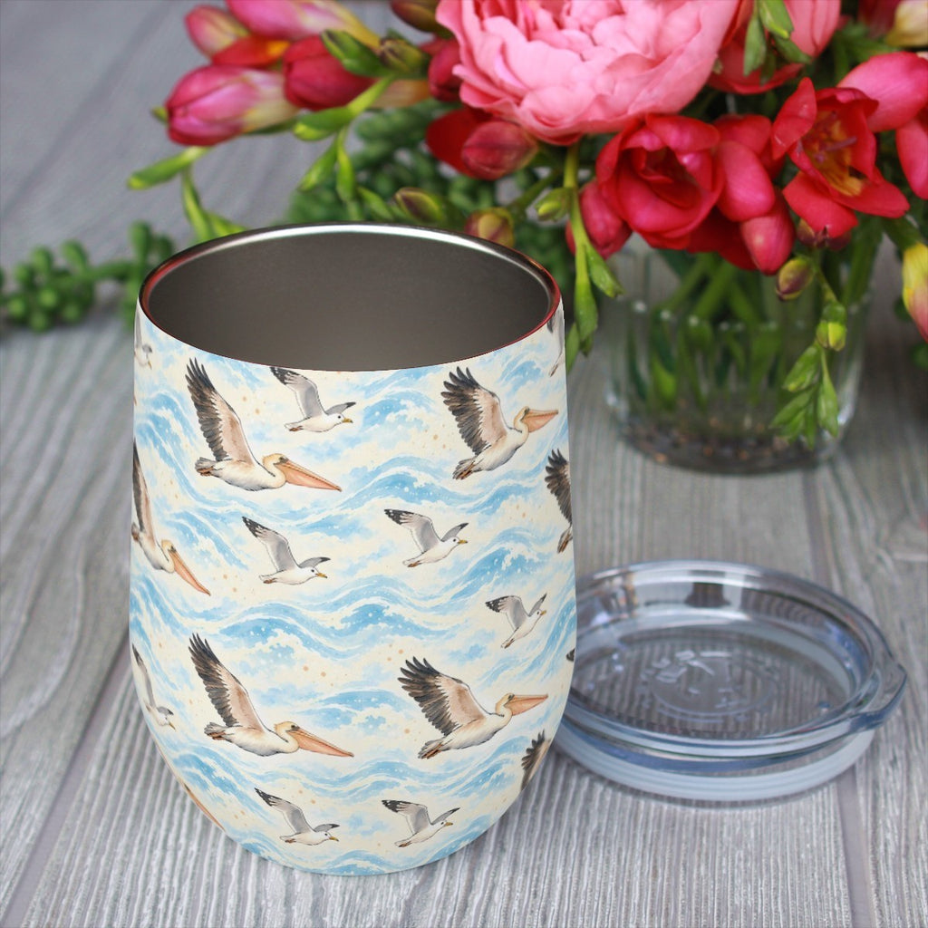 Pelican pattern tumbler with its clear lid beside it on a wooden table, red flowers in the background