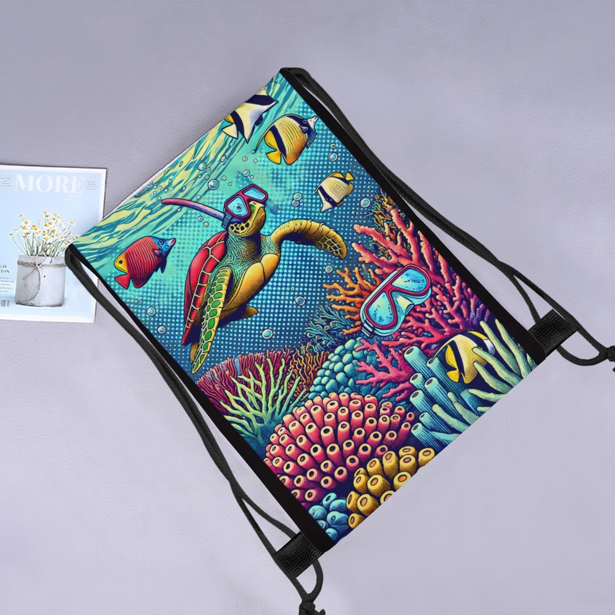 Snorkelling turtle drawstring bag laid flat next to a magazine and flowers.
