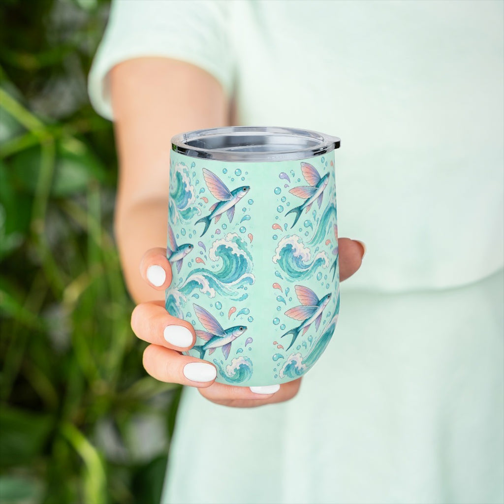 Hand holding the flying fish pattern tumbler in front of green leaves, with a pale green top behind