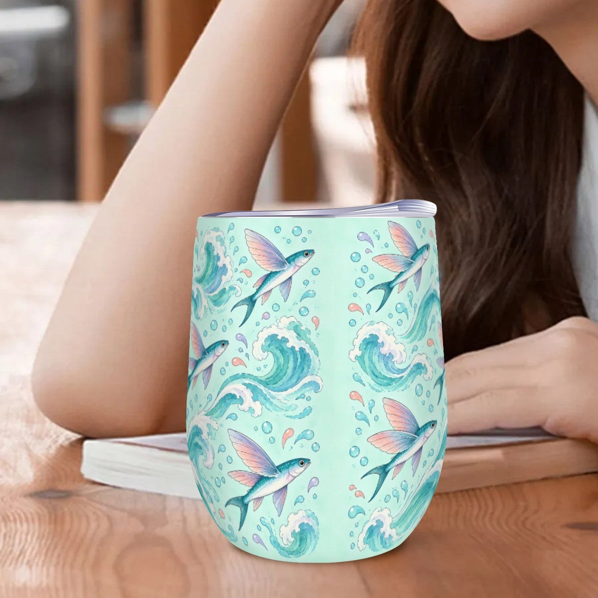Flying fish tumbler standing on a wooden table beside a woman resting her arm