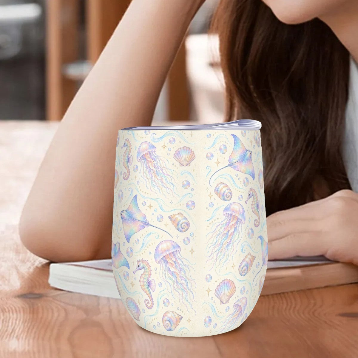 Jellyfish and seahorse tumbler standing on a wooden table beside a woman resting her arm