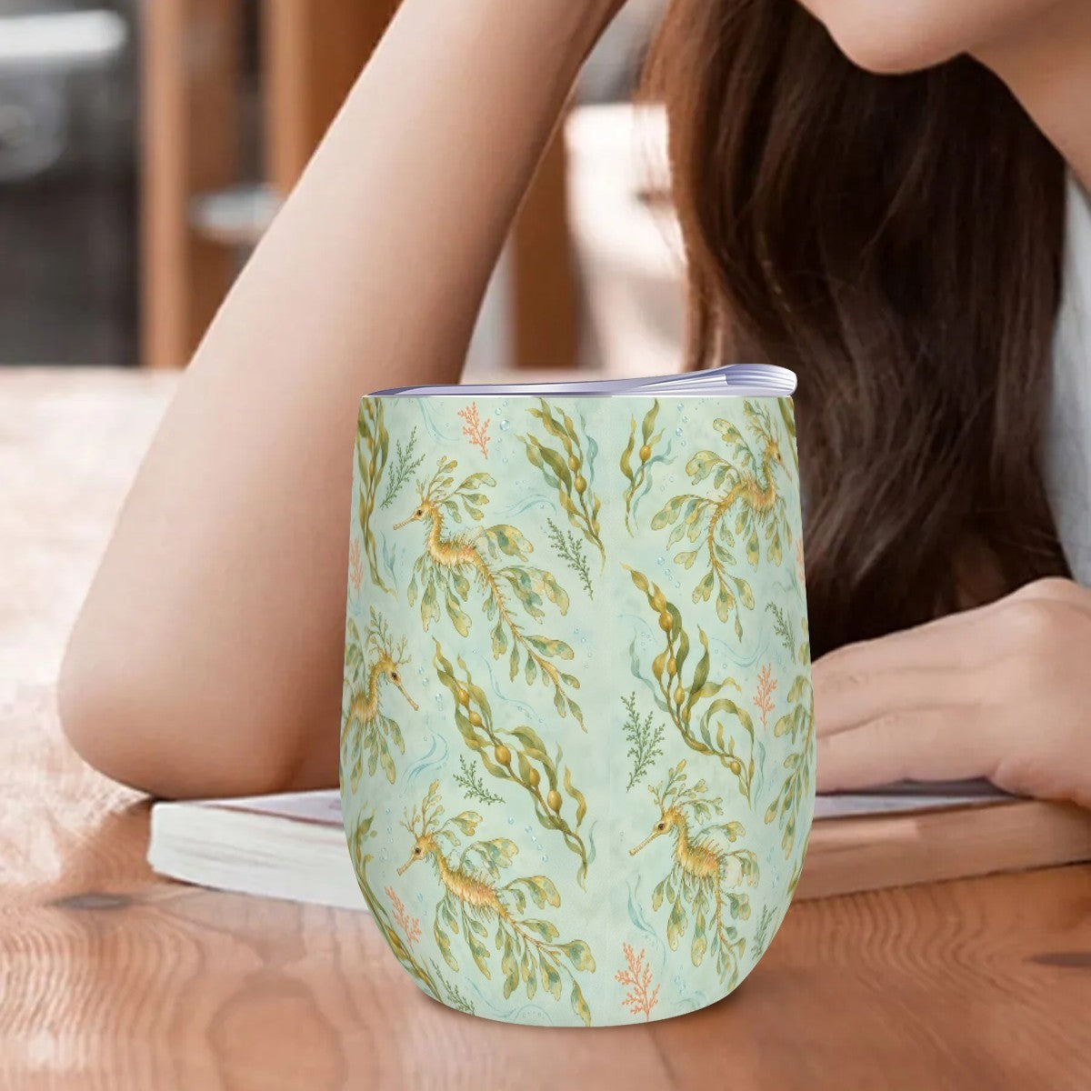 Leafy sea dragon tumbler standing on a wooden table beside a woman resting her arm