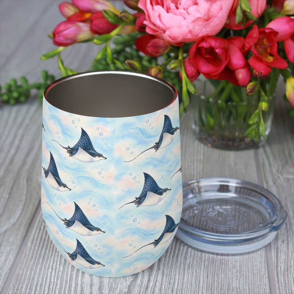 Eagle ray pattern tumbler with its clear lid beside it on a wooden table, red flowers in the background