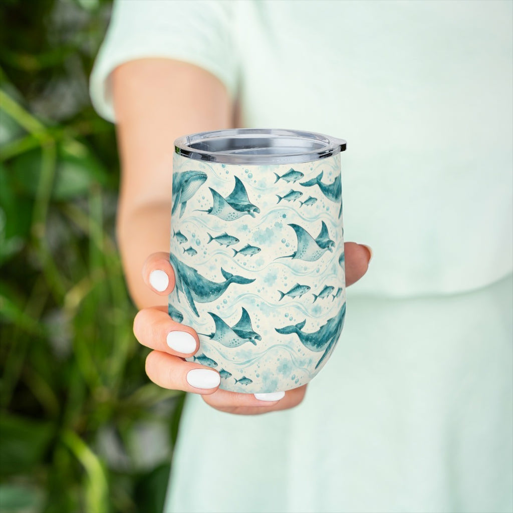 Hand holding the whale and ray pattern tumbler in front of green leaves, with a pale green top behind