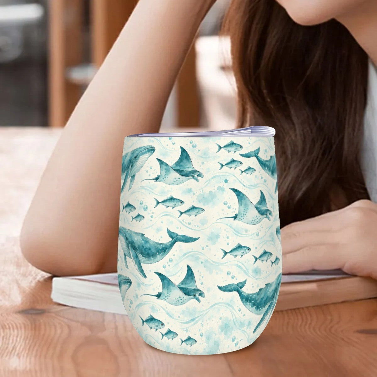 Whale and ray tumbler standing on a wooden table beside a woman resting her arm