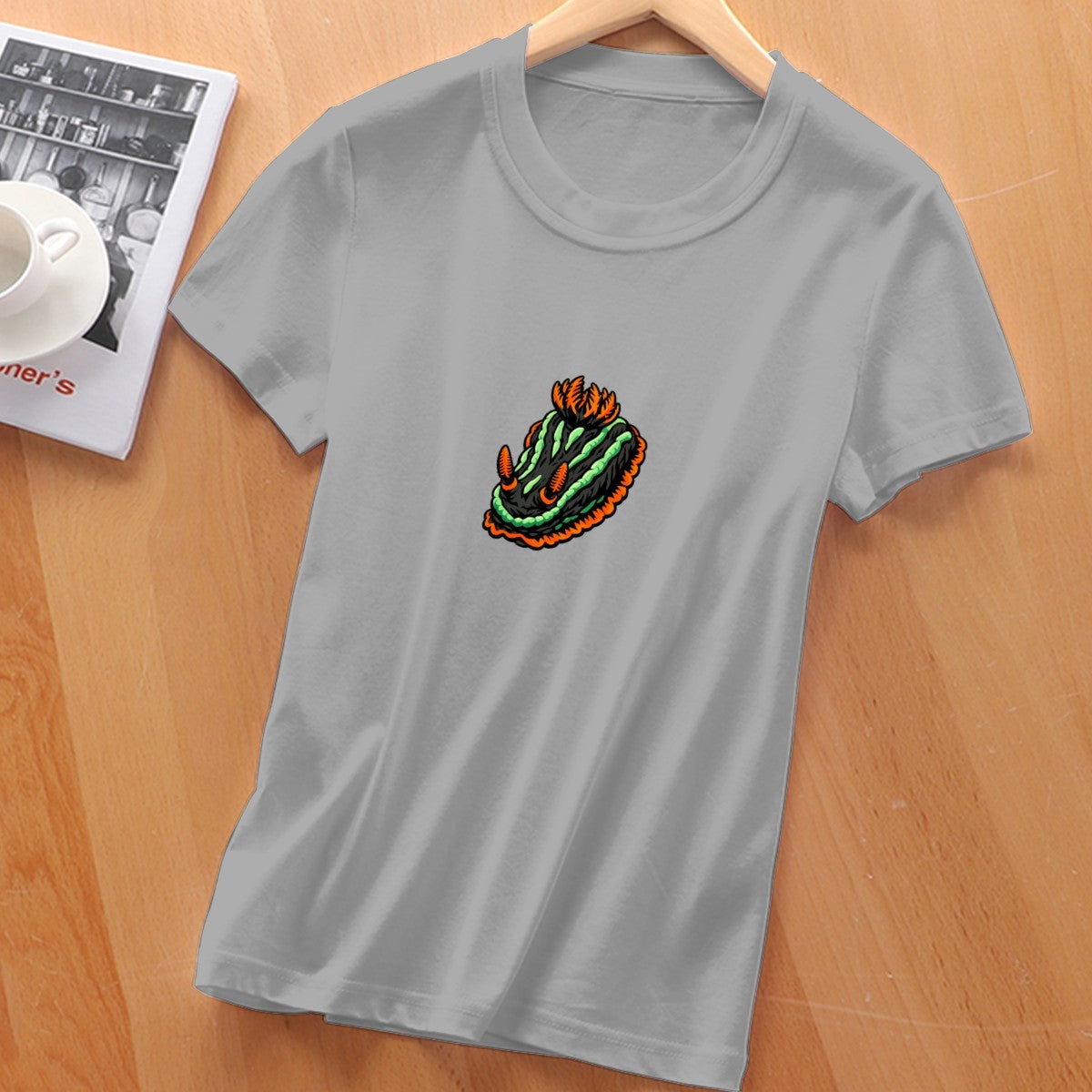 Silver grey Nembrotha nudibranch tee laid flat on a wooden table, front