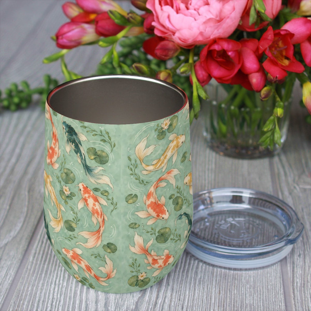 Koi pattern tumbler with its clear lid beside it on a wooden table, red flowers in the background