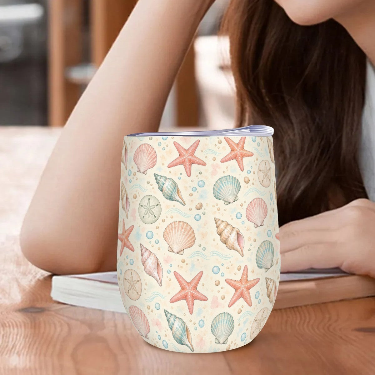 Seashell tumbler standing on a wooden table beside a woman resting her arm