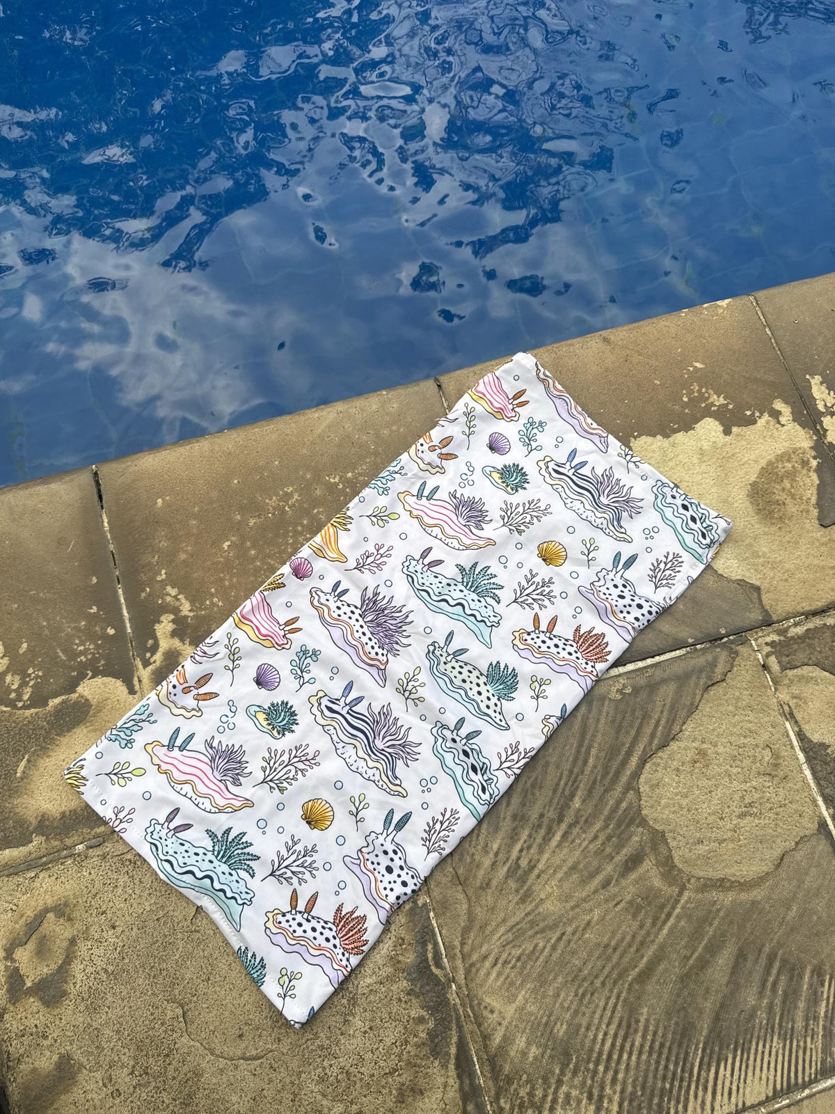 Pastel nudibranch neck gaiter laid flat beside a swimming pool to show the print