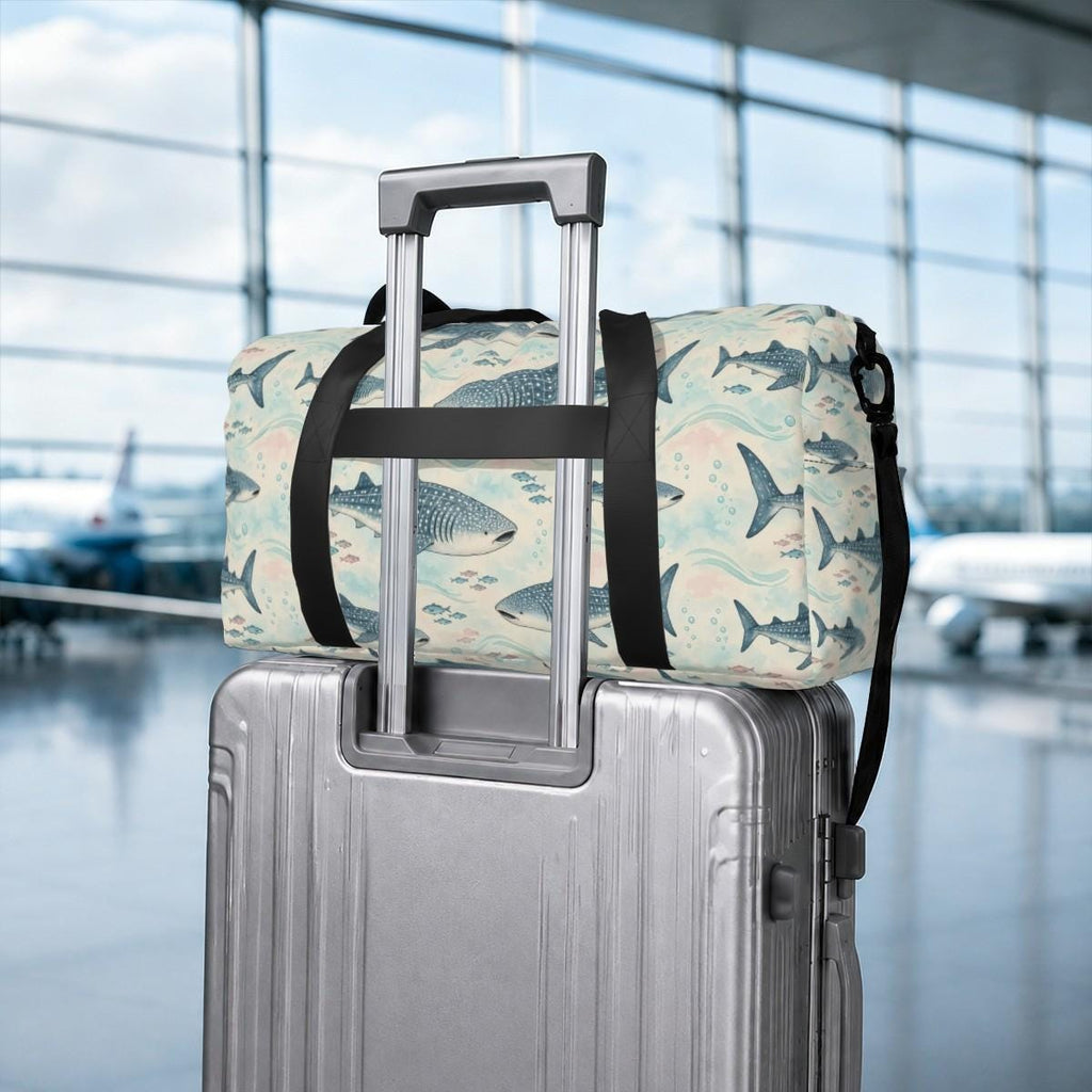 Whale shark duffle bag slung over the handle of a silver suitcase in an airport
