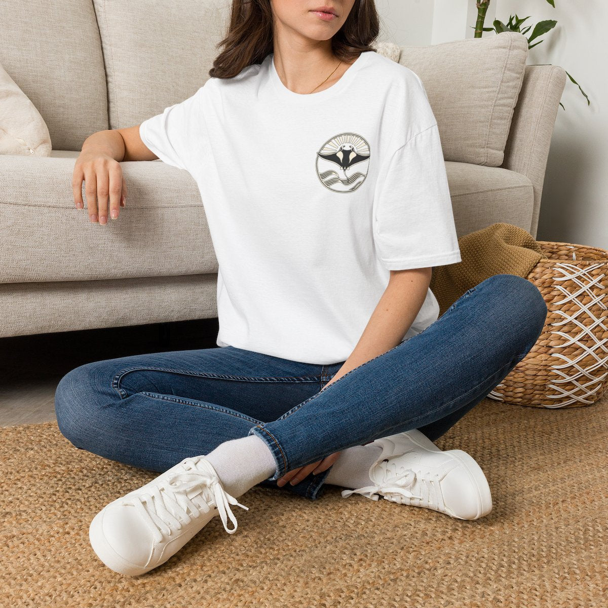 Woman sitting on the floor in a white t-shirt with a small manta ray sunrise badge on the chest, digital mockup