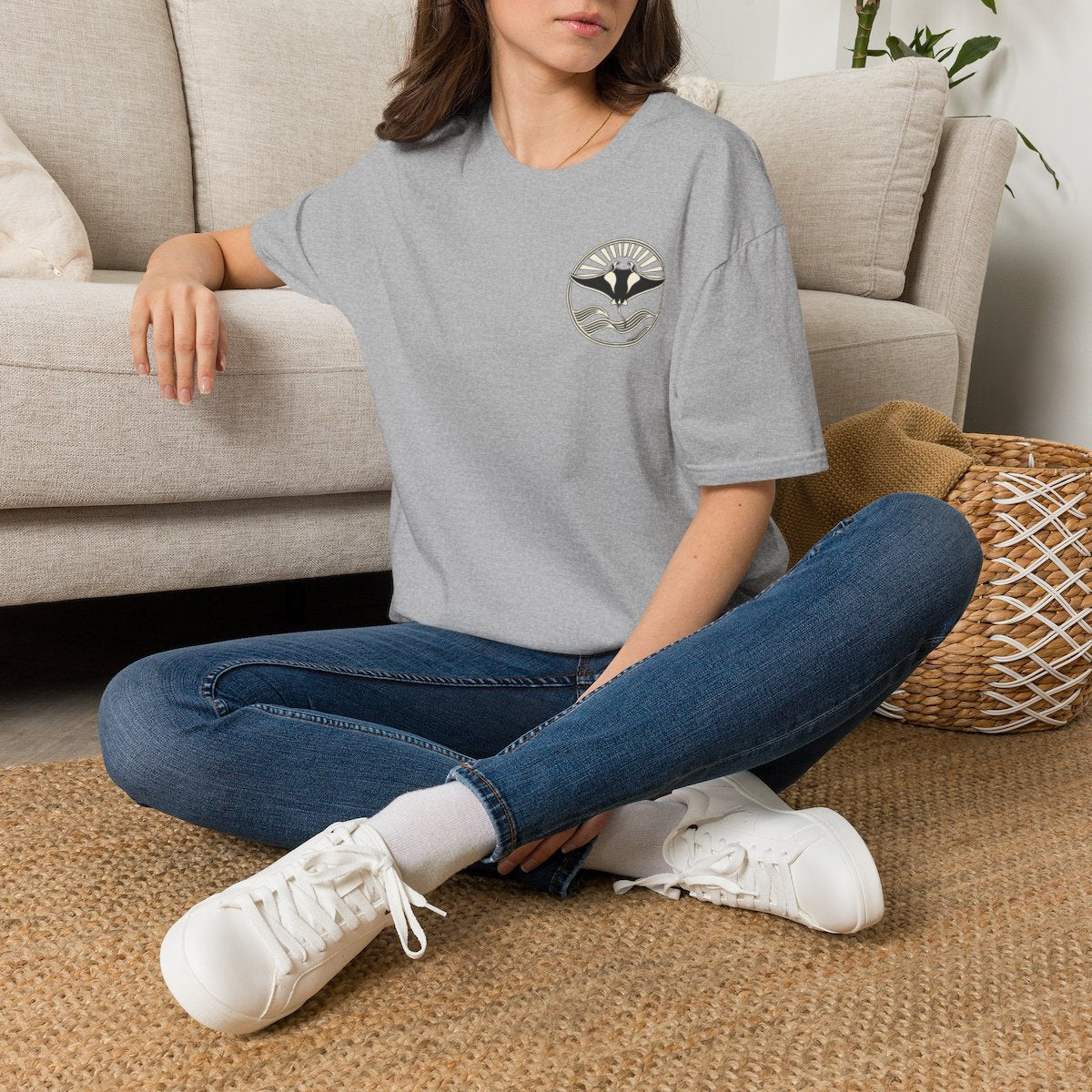 Woman sitting on the floor in a sport grey t-shirt with a small manta ray sunrise badge on the chest, digital mockup