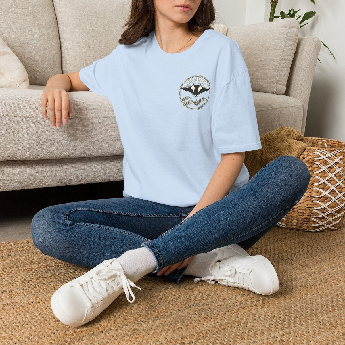 Woman sitting on the floor in a light blue t-shirt with a small manta ray sunrise badge on the chest, digital mockup